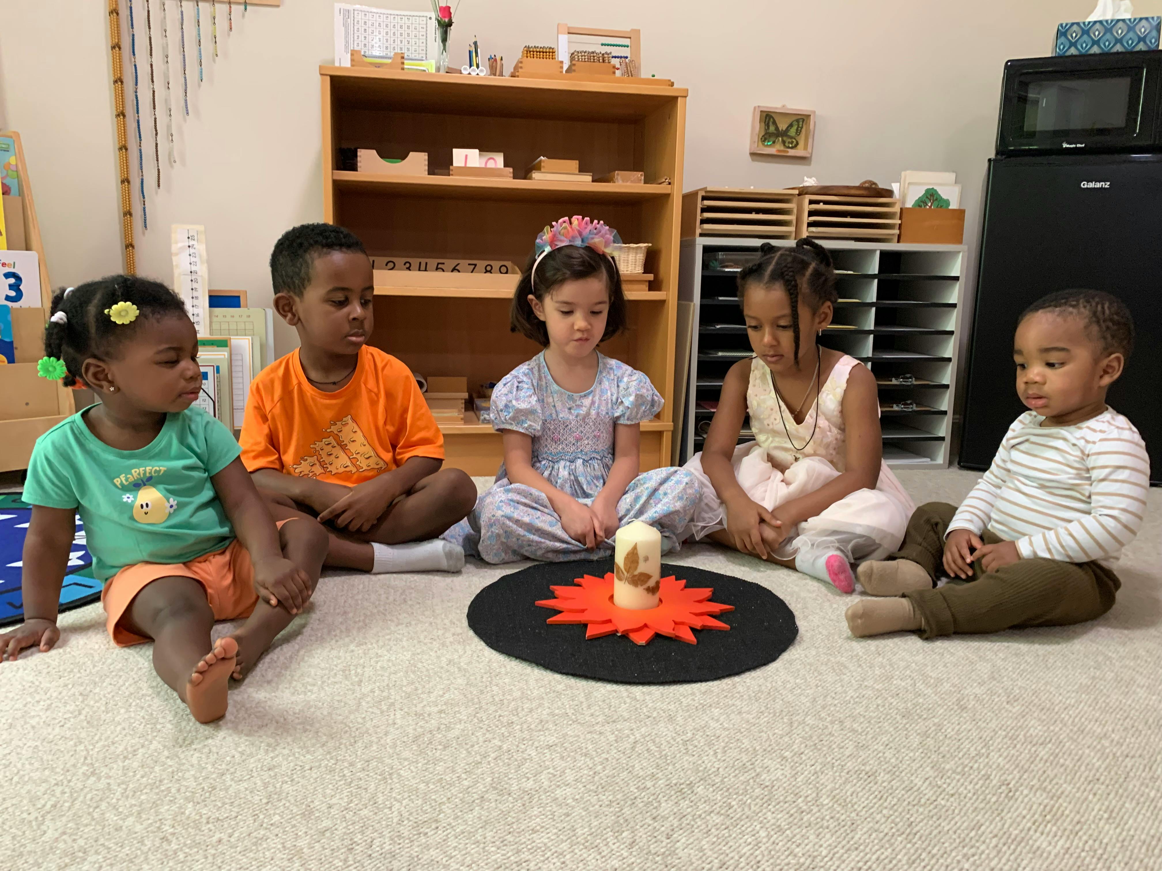 Five children sitting in a circle around a candle on a classroom floor