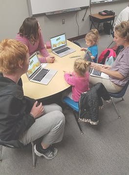 Adults and children sitting around a table with laptops