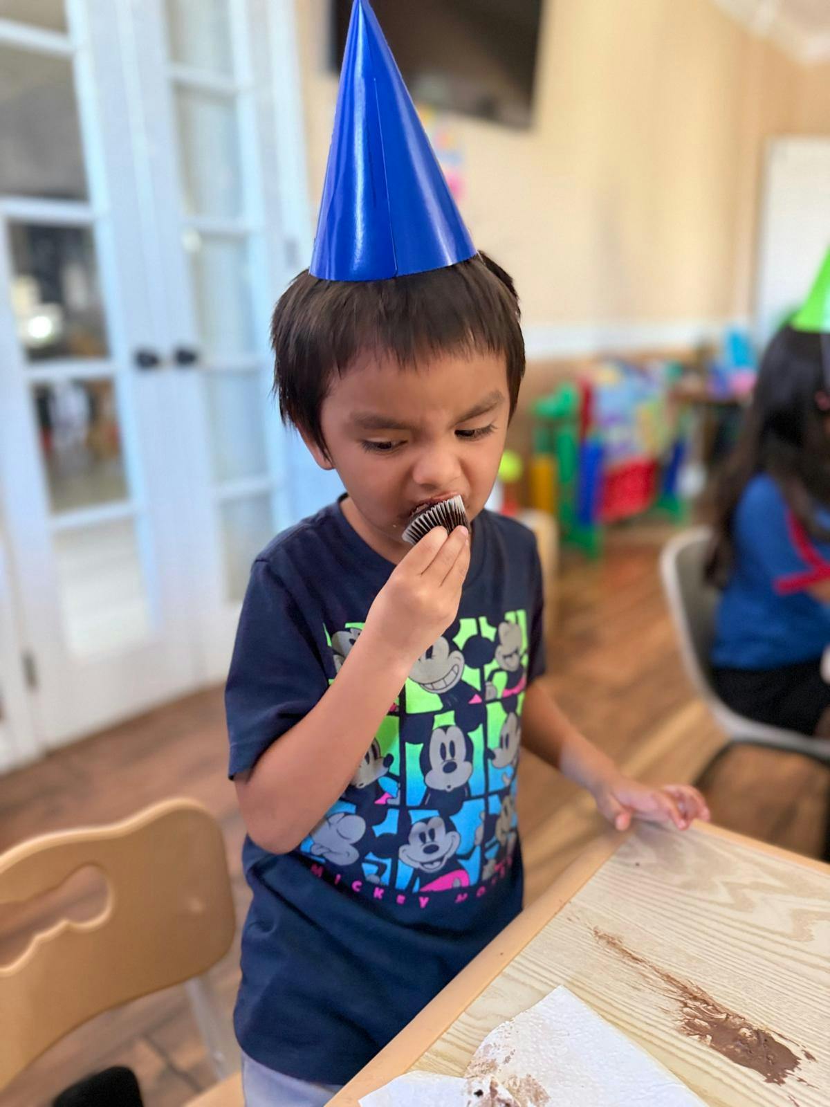 Child wearing a party hat eating a cupcake