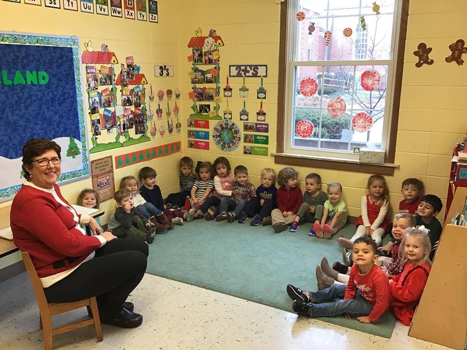 Adult sitting in a chair with children sitting on the floor in a classroom