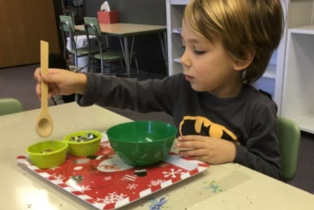 Child holding a wooden spoon over small bowls