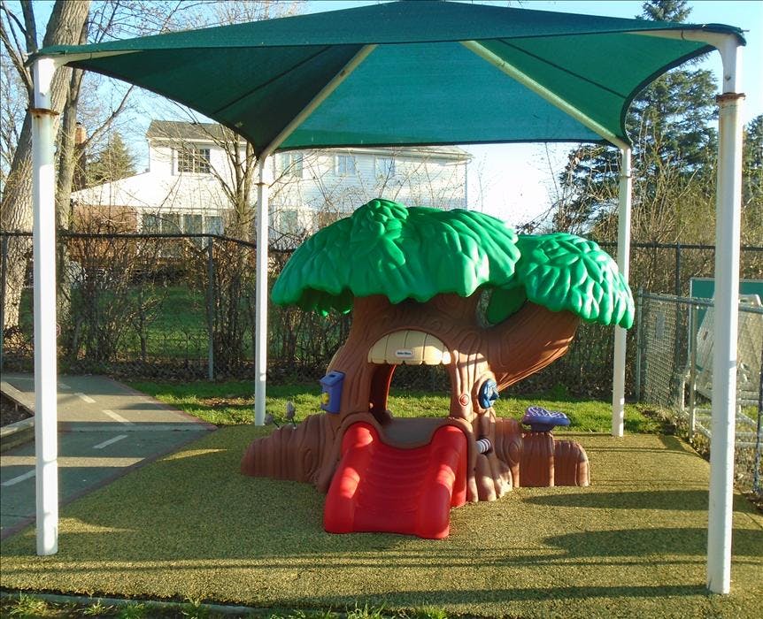 Playground with a treehouse slide and a green shade canopy over artificial turf