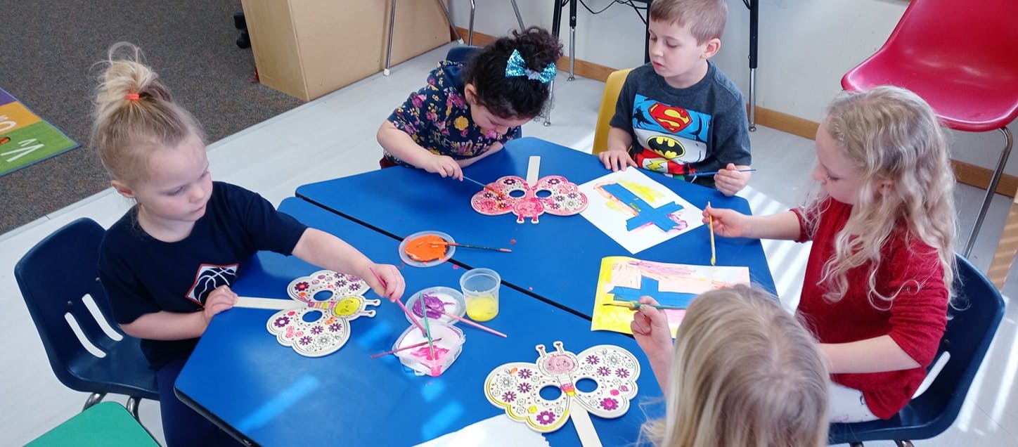 Children painting butterfly crafts at a blue table