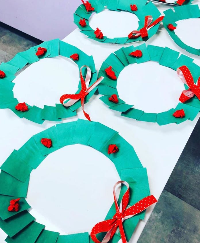 Multiple green paper wreaths with red bows and accents