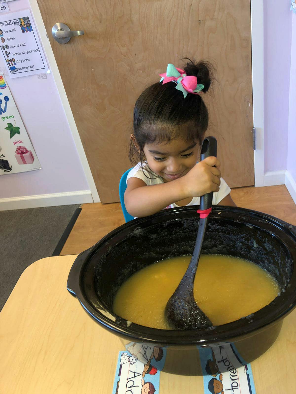 Child stirring a large pot of yellow liquid with a ladle