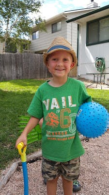 Child in a hat holding a blue ball and a toy shovel
