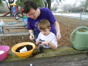Adult and child planting in small pots on a picnic table
