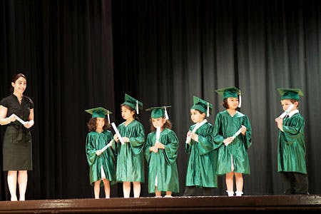 Person with children in graduation caps and gowns on a stage