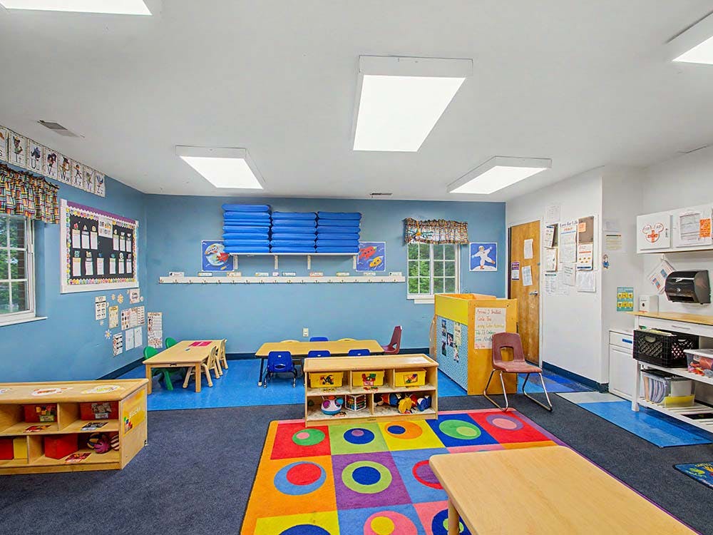 Colorful classroom with small tables, chairs, shelves, and a rug