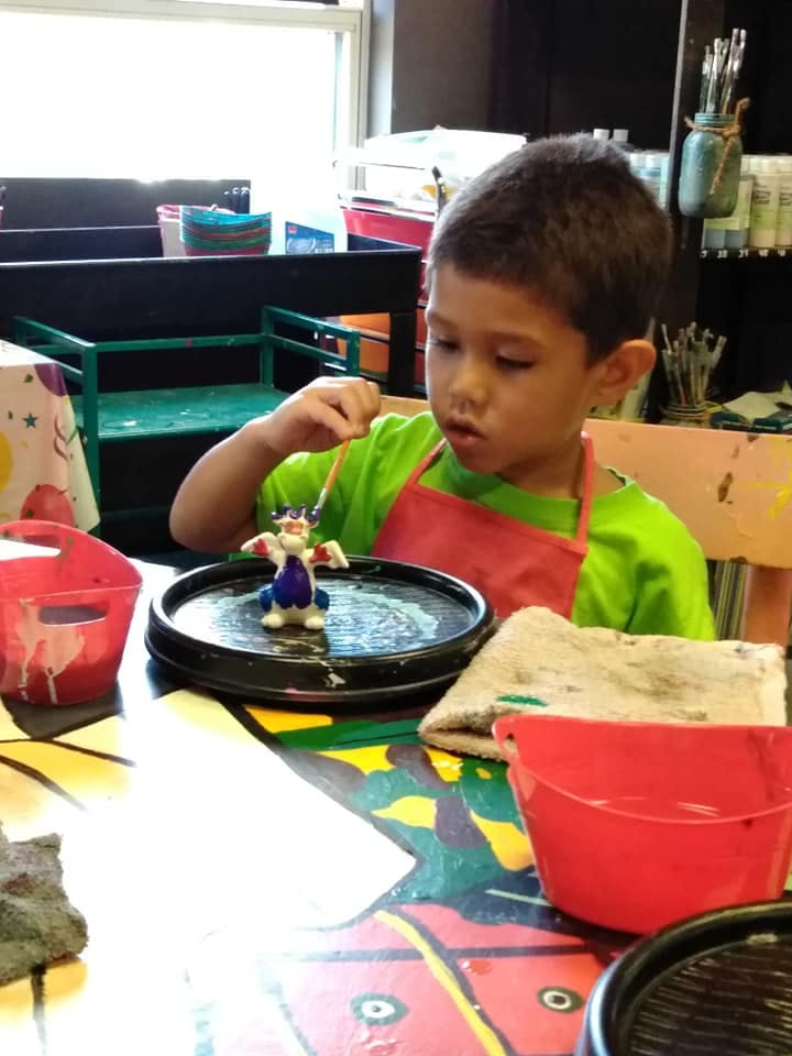 Child in an apron painting a small figurine