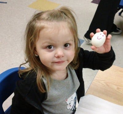 Child holding up an egg with a drawn face