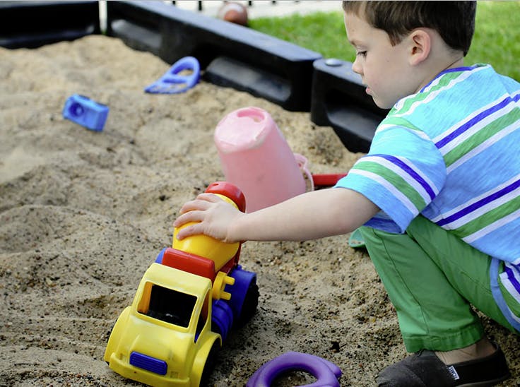 Child playing with a toy truck in a sandbox
