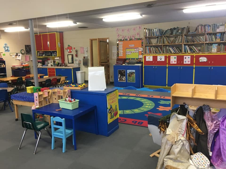 Classroom with blue and red furniture, bookshelves, and a colorful rug