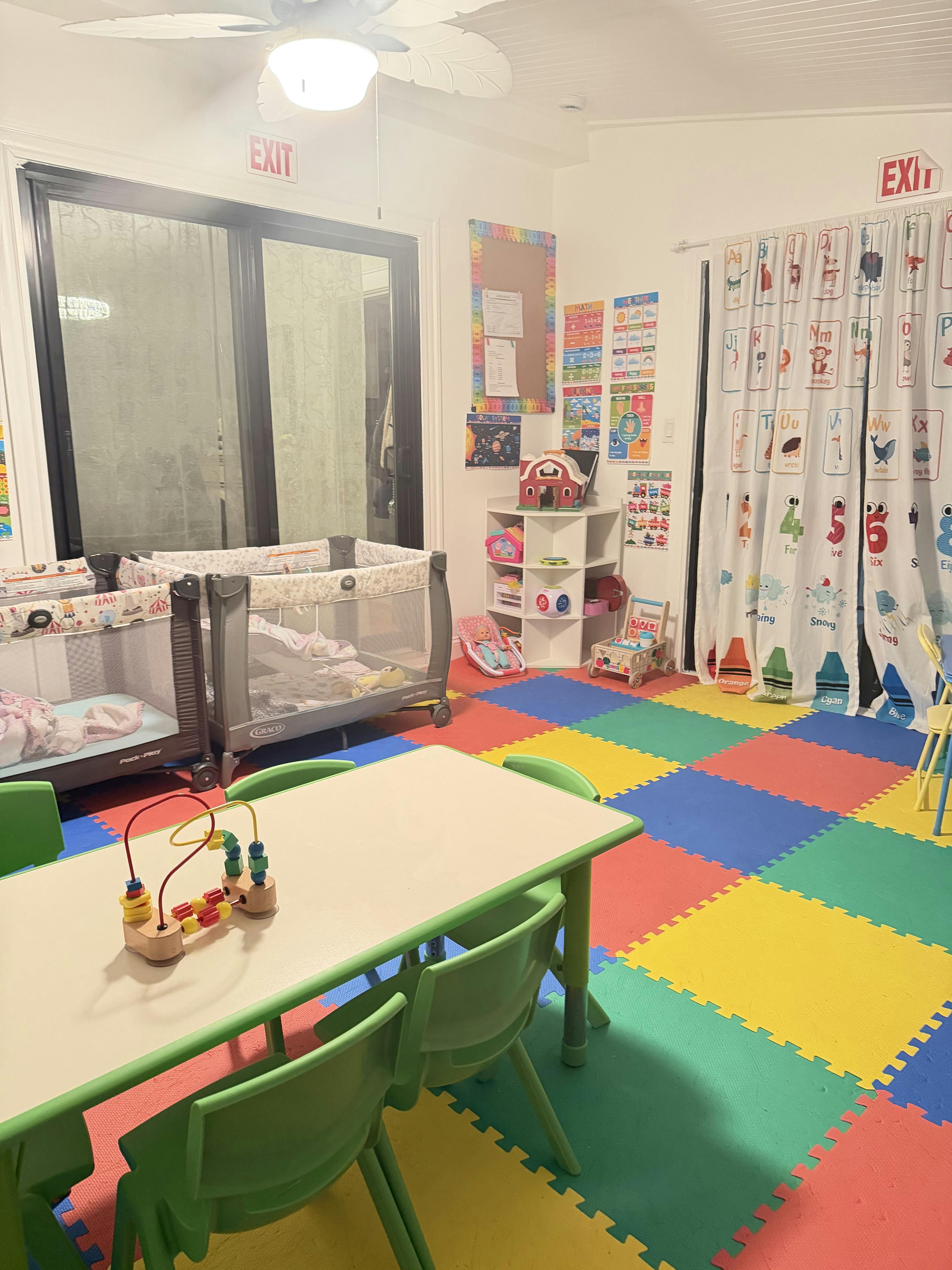 Colorful play area with playpens, table, chairs, and educational wall charts