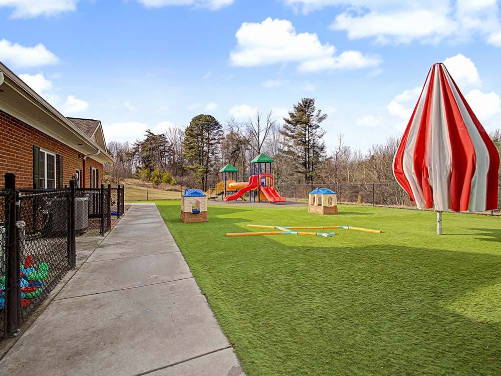 Outdoor playground with artificial turf, play structures, and a large umbrella