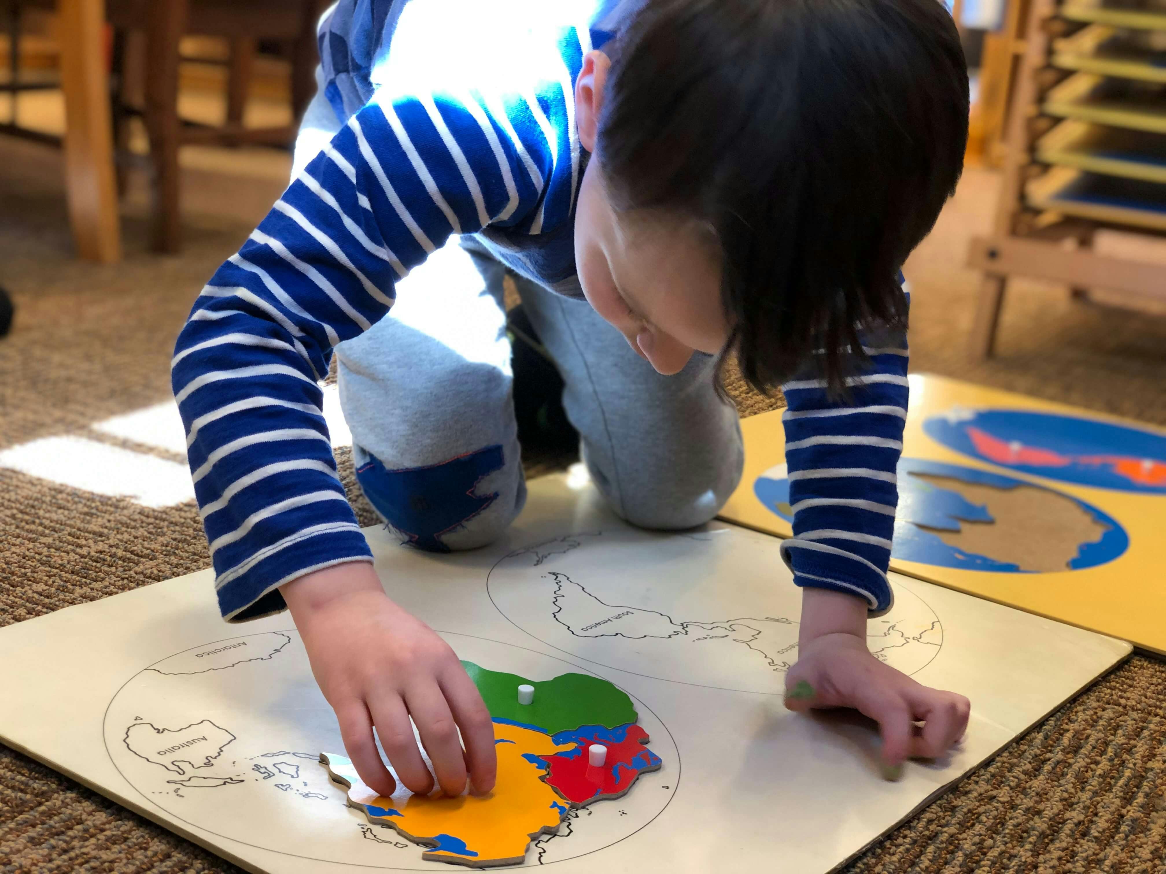 Child kneeling and placing a puzzle piece on a map