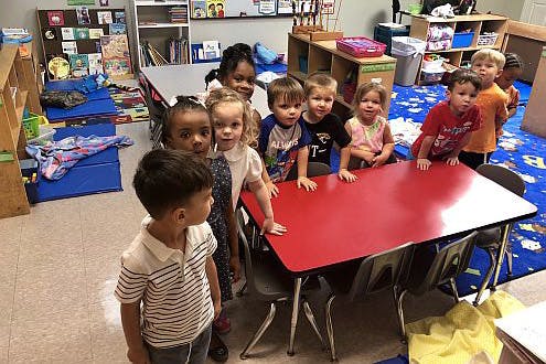 Group of children standing around a red table in a classroom