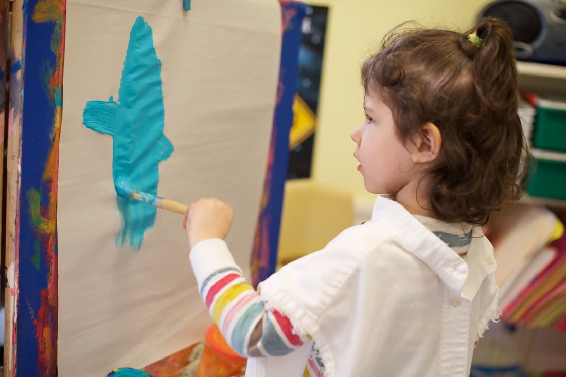 Child painting a blue shape on an easel
