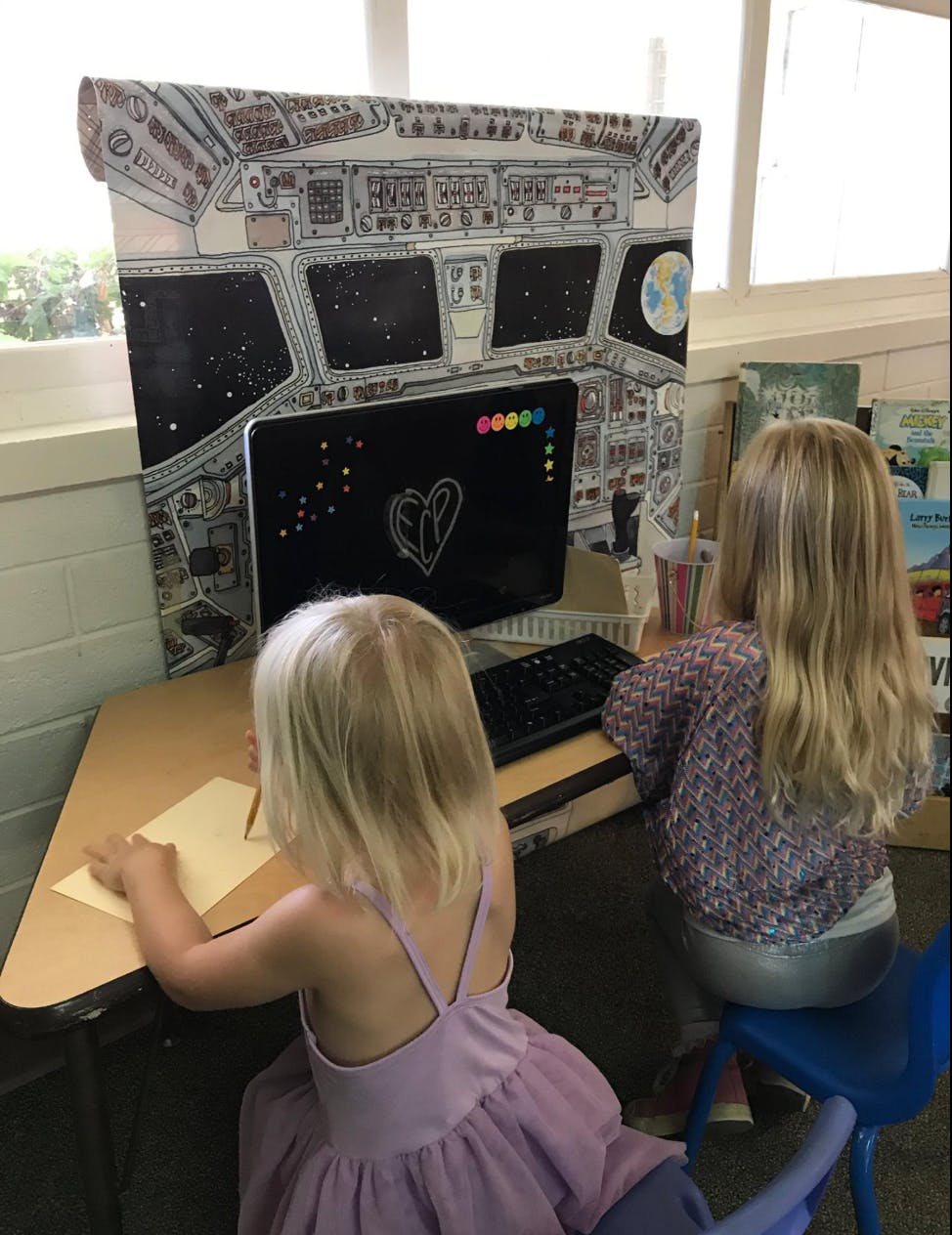 Two children at a desk with a space shuttle cockpit backdrop
