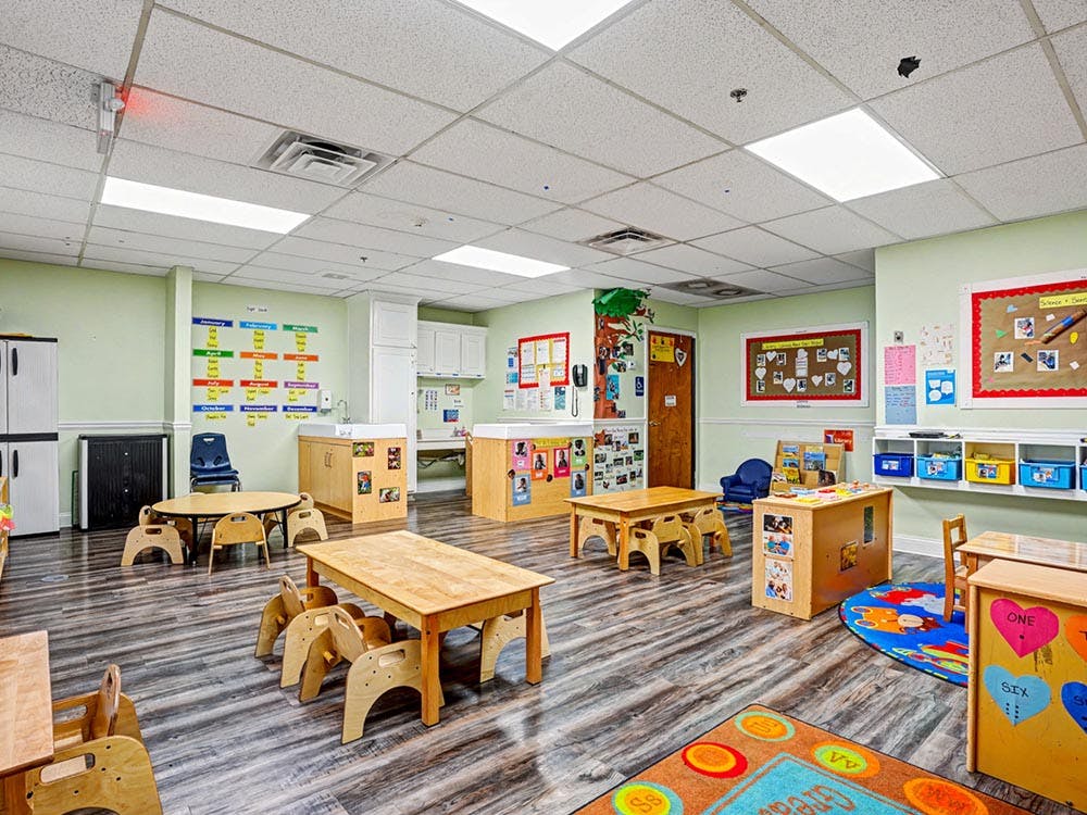 Classroom with small wooden tables and chairs, light green walls, and various educational posters