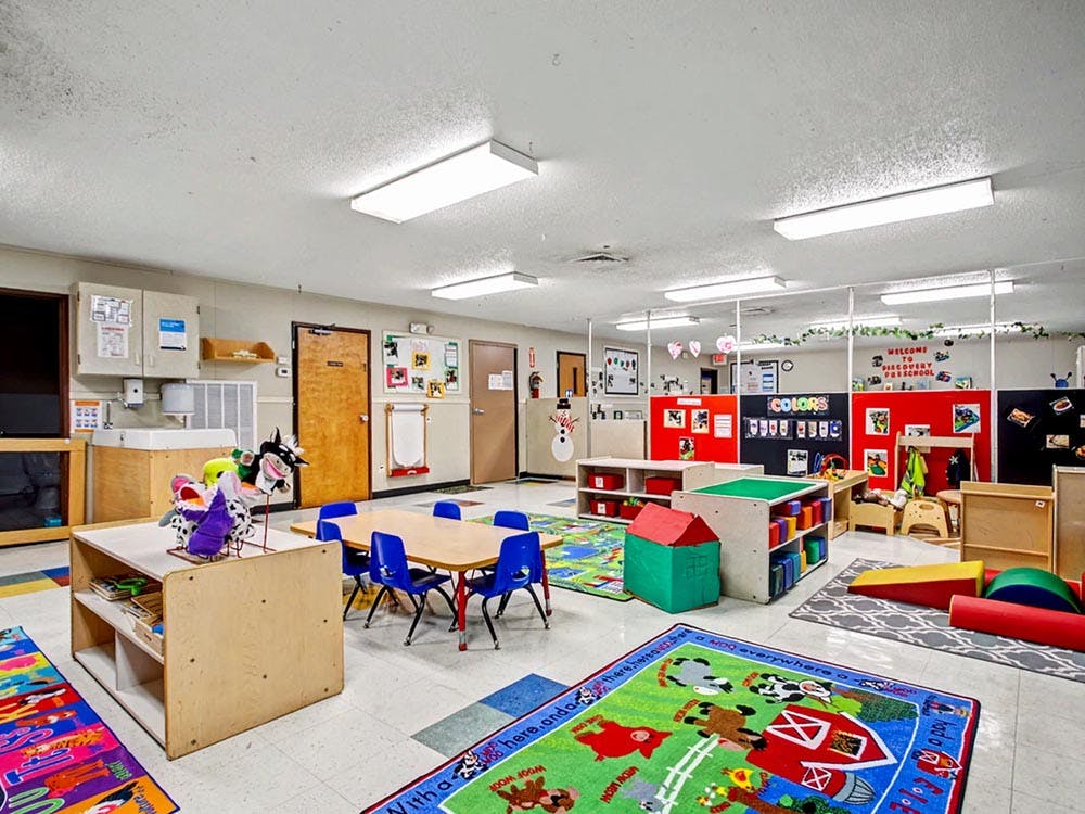 A colorful classroom with small tables and chairs, play mats, and learning stations