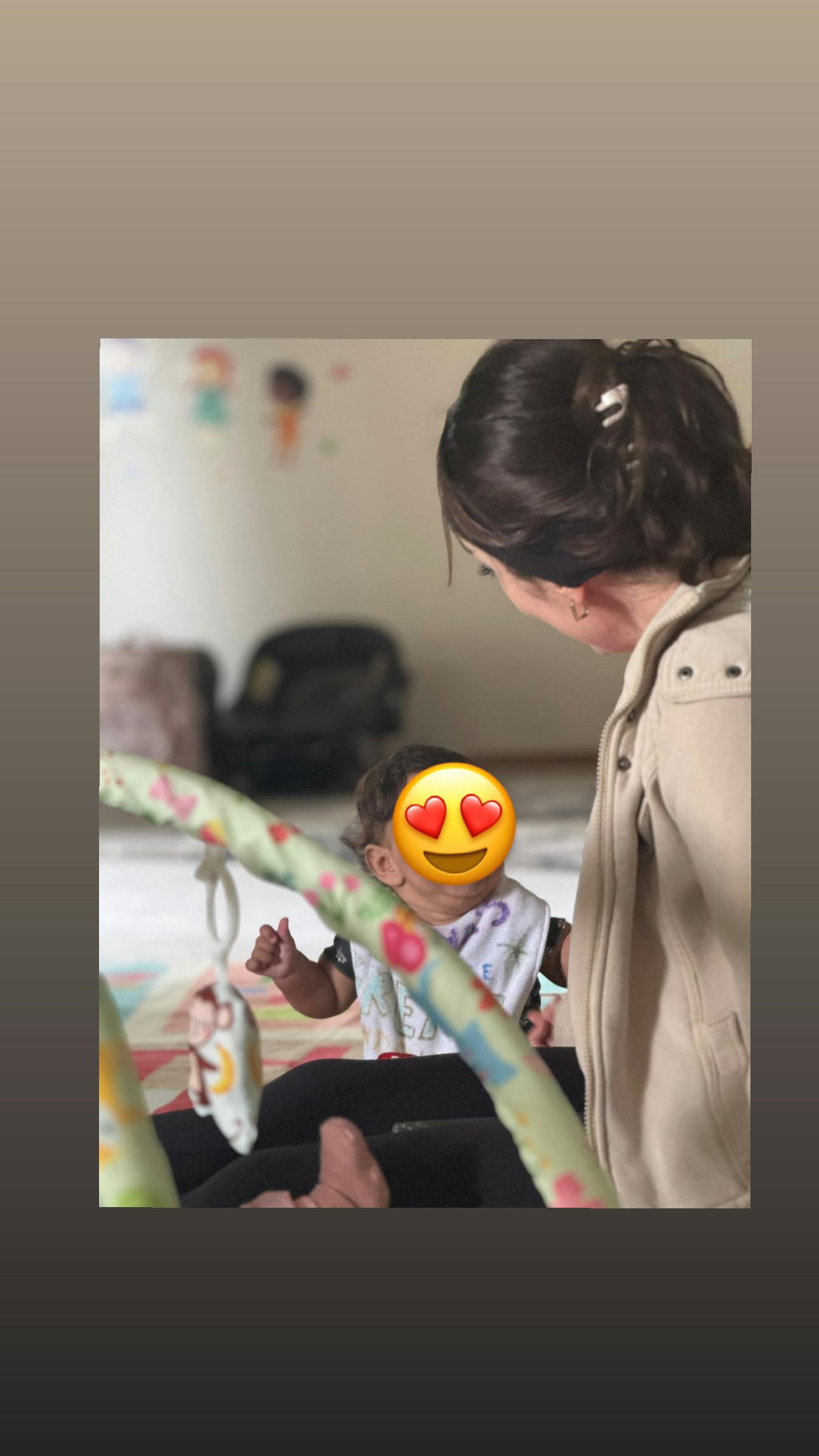 Adult person interacting with a child wearing a bib near a playmat