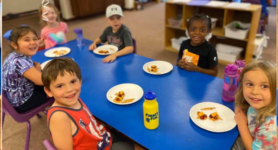 Children sitting at a blue table with plates of food