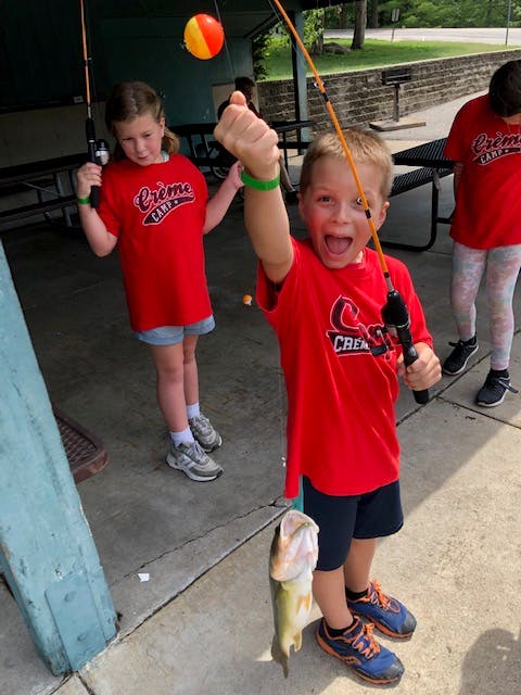 Child holding fishing rod with fish on the ground
