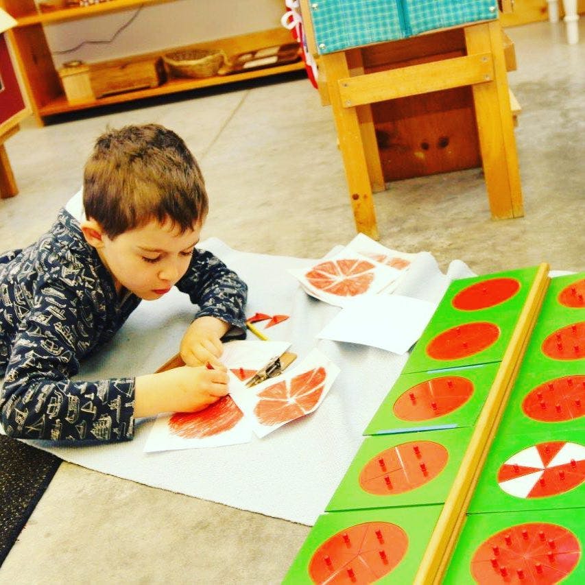 Child on floor working with paper cutouts and a learning board