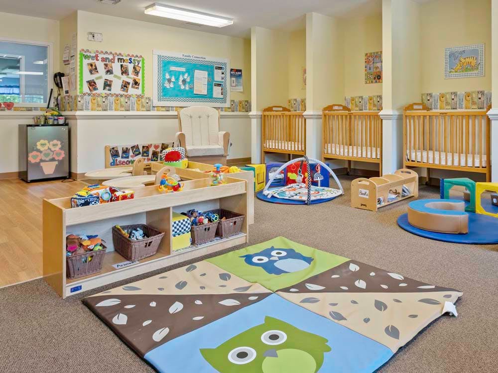 Playroom with cribs, playmats, shelves with toys, and an armchair