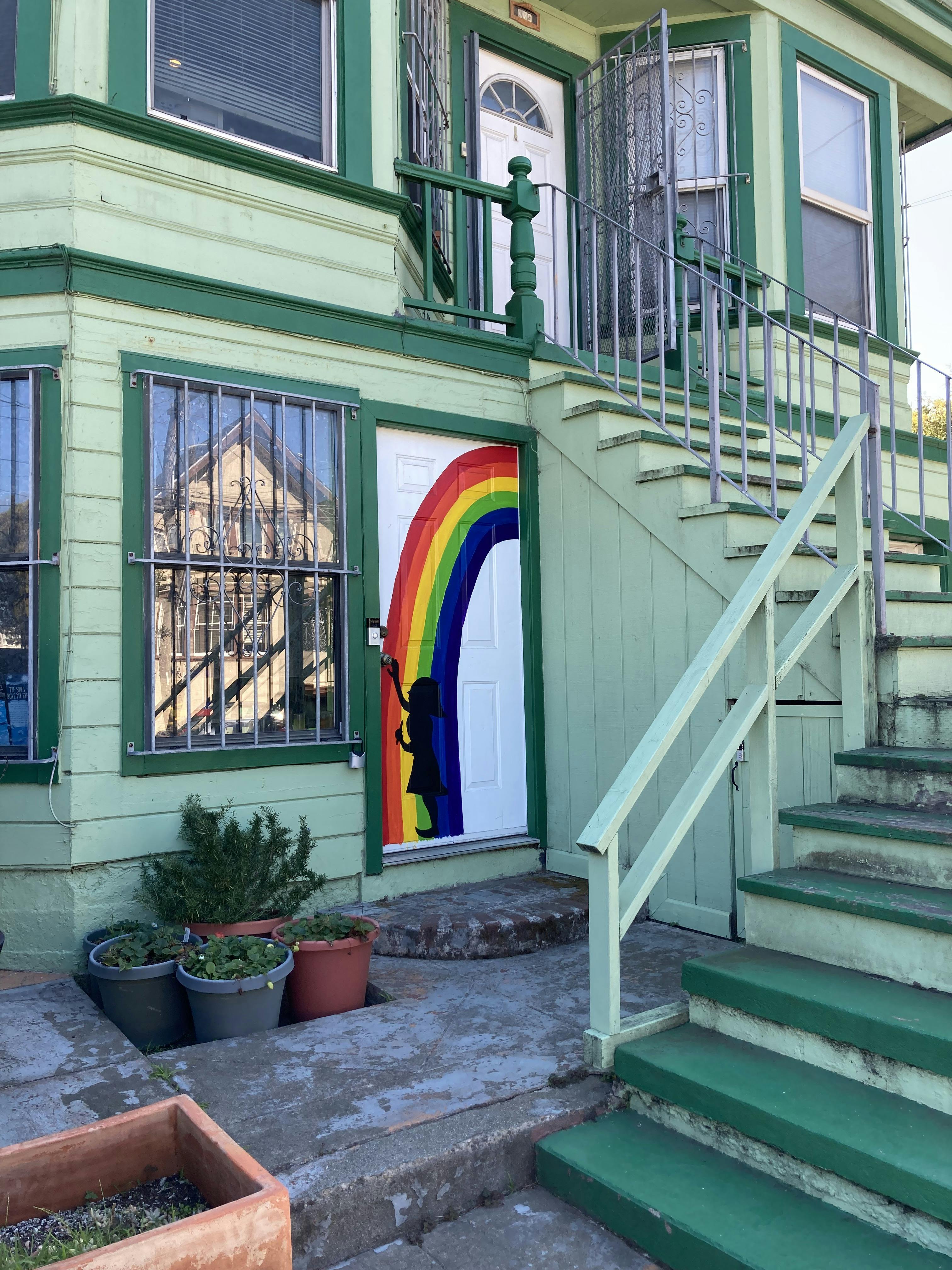 Green house with a white door painted with a rainbow arch and a child's silhouette