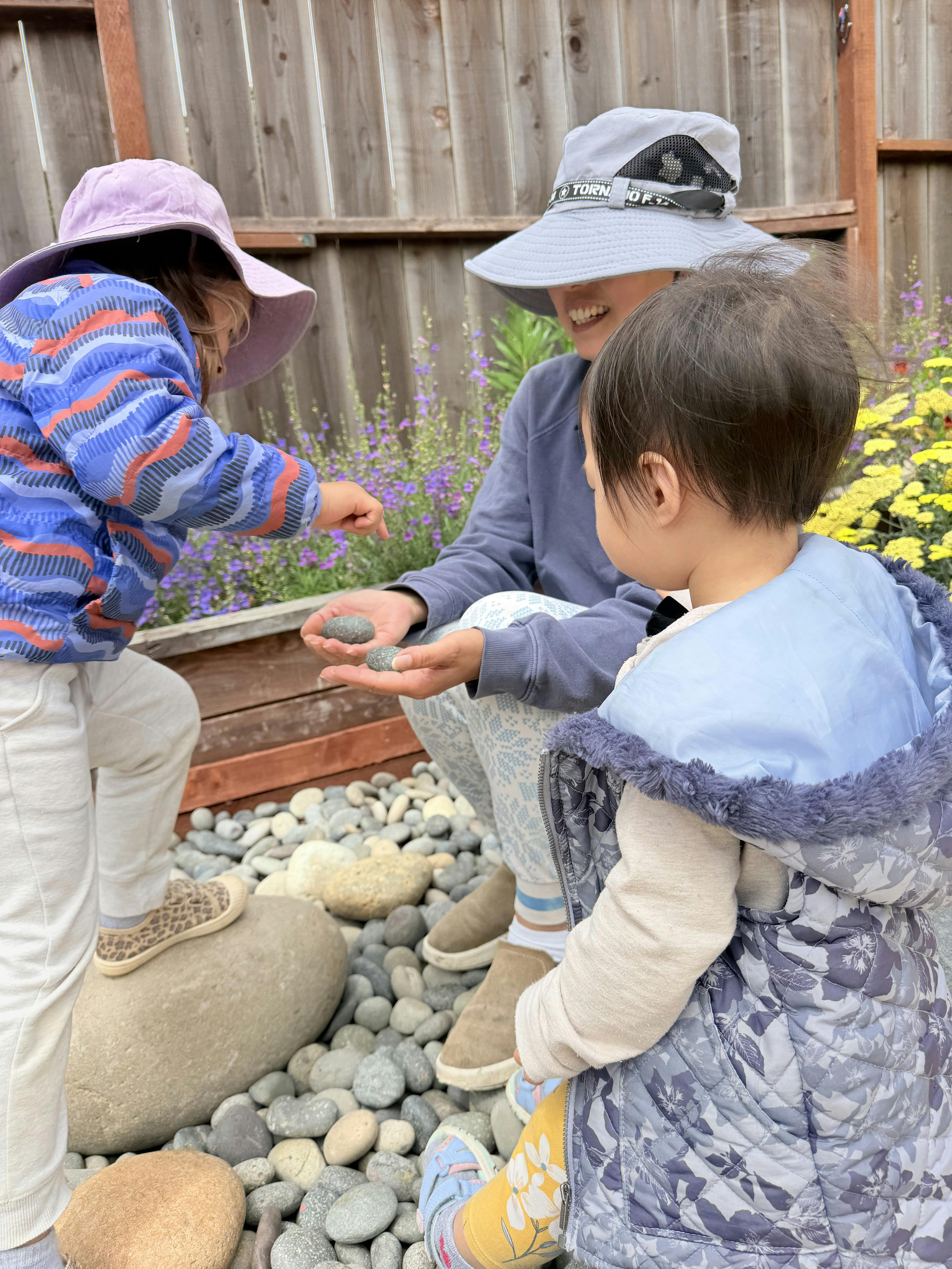 A person and two children interacting with rocks in a garden