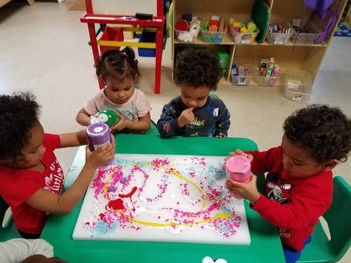 Four children at a table playing with colorful materials