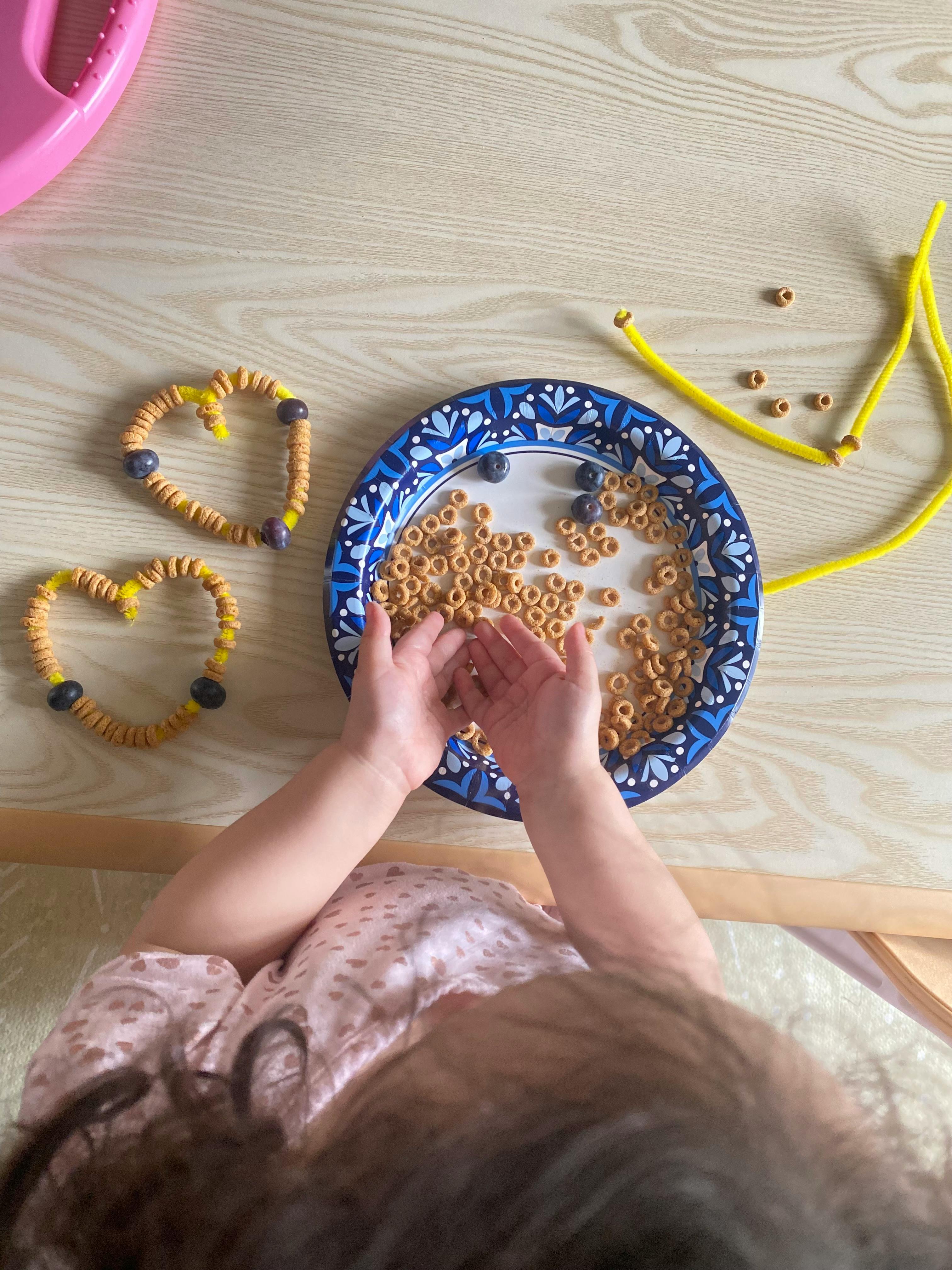 Child crafting heart shapes with cereal and blueberries on a table