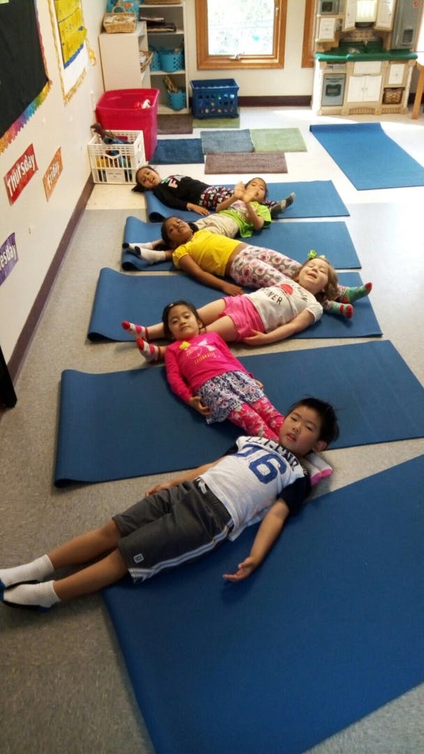 Children lying on blue mats in a classroom