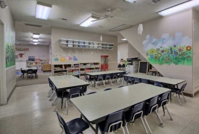 Classroom with multiple tables and chairs, shelves, and a wall mural