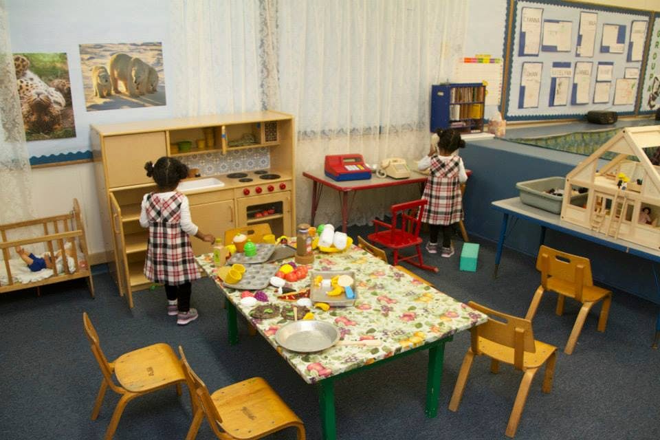 Two children playing in a classroom with a play kitchen and table
