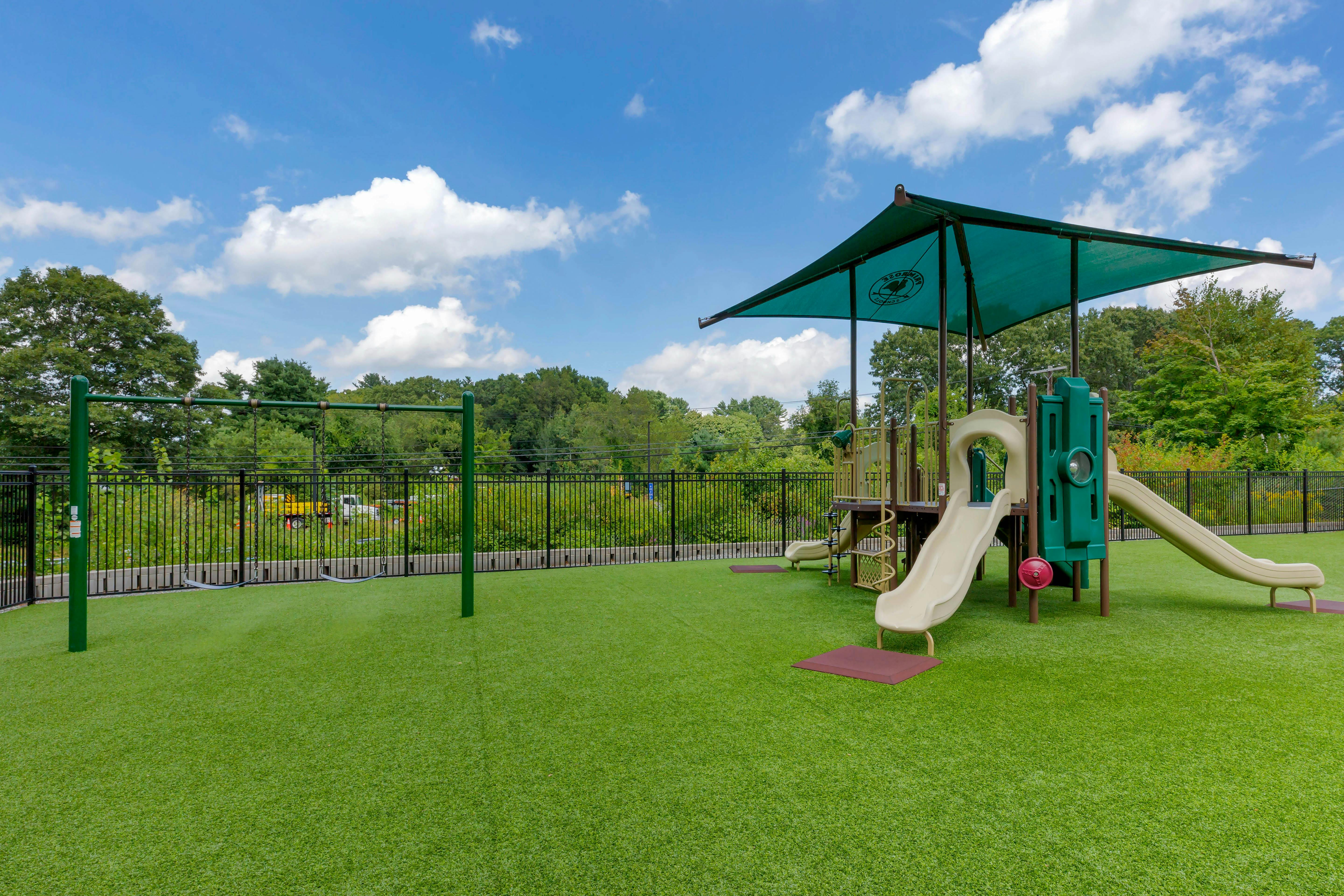 A green astroturf playground with a swing set and a jungle gym with slides
