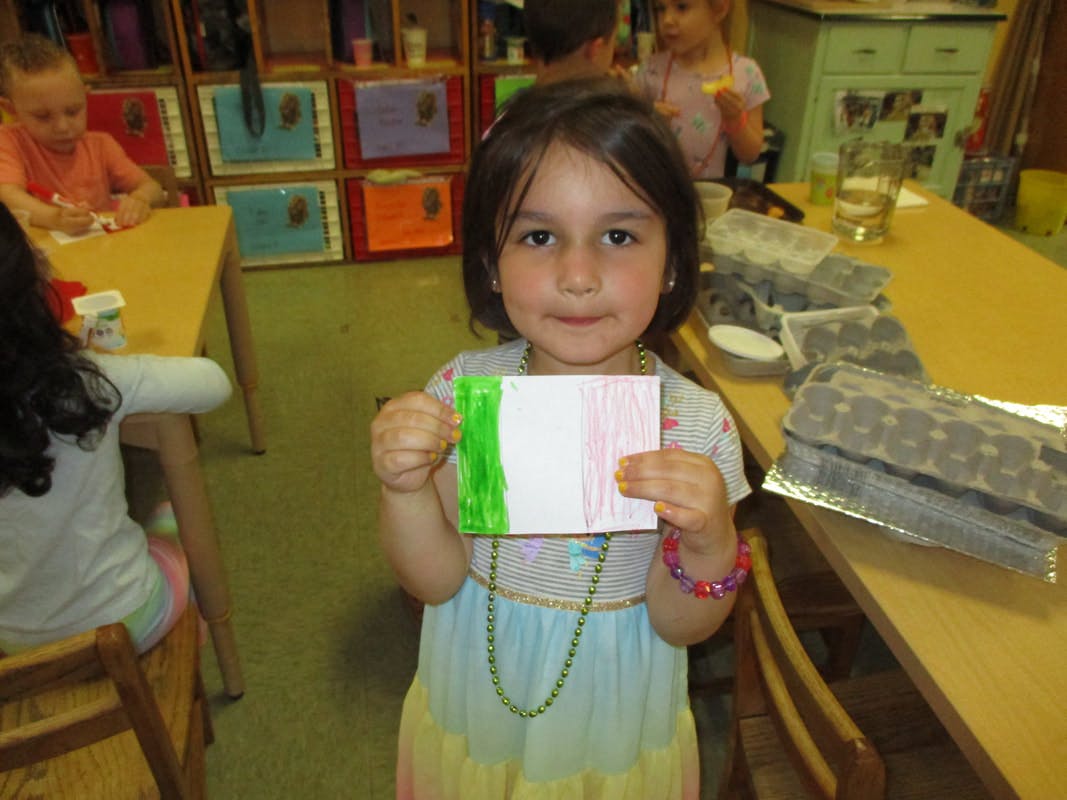 Child holding up a small drawing with green and pink stripes