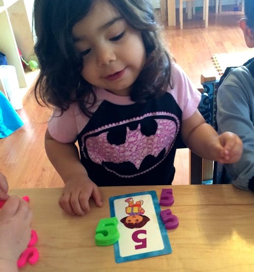 Child playing with number five card and number shapes