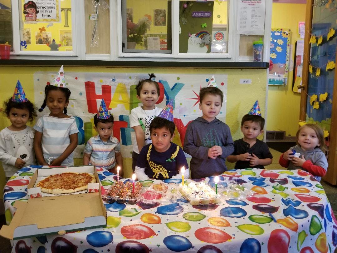 Group of children in party hats around a table with pizza and cake