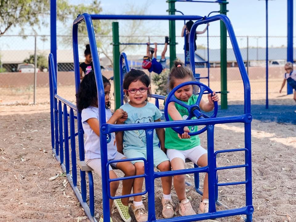Children playing on a blue playground structure with a steering wheel