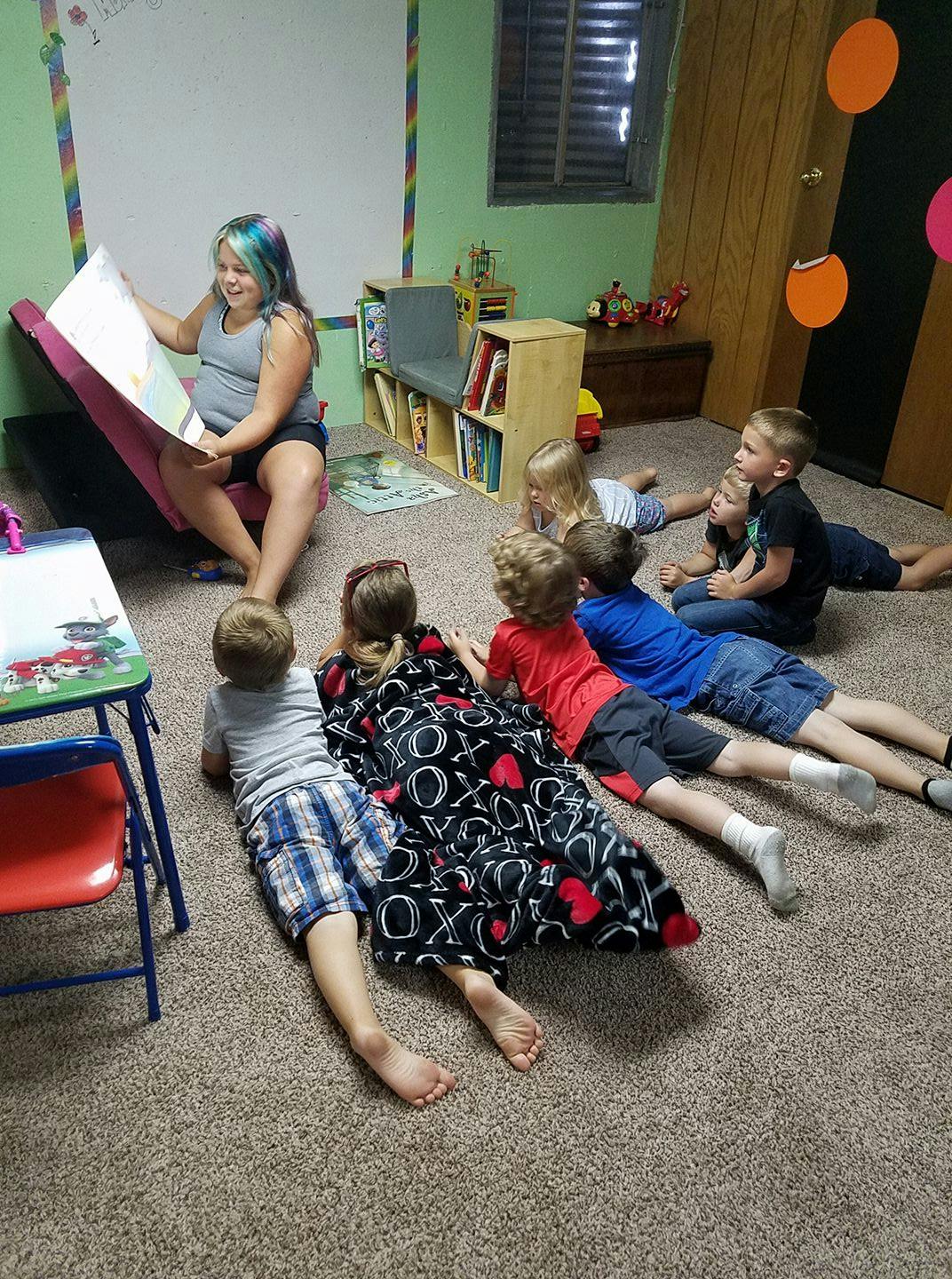 Person reading a book to several children lying on the floor