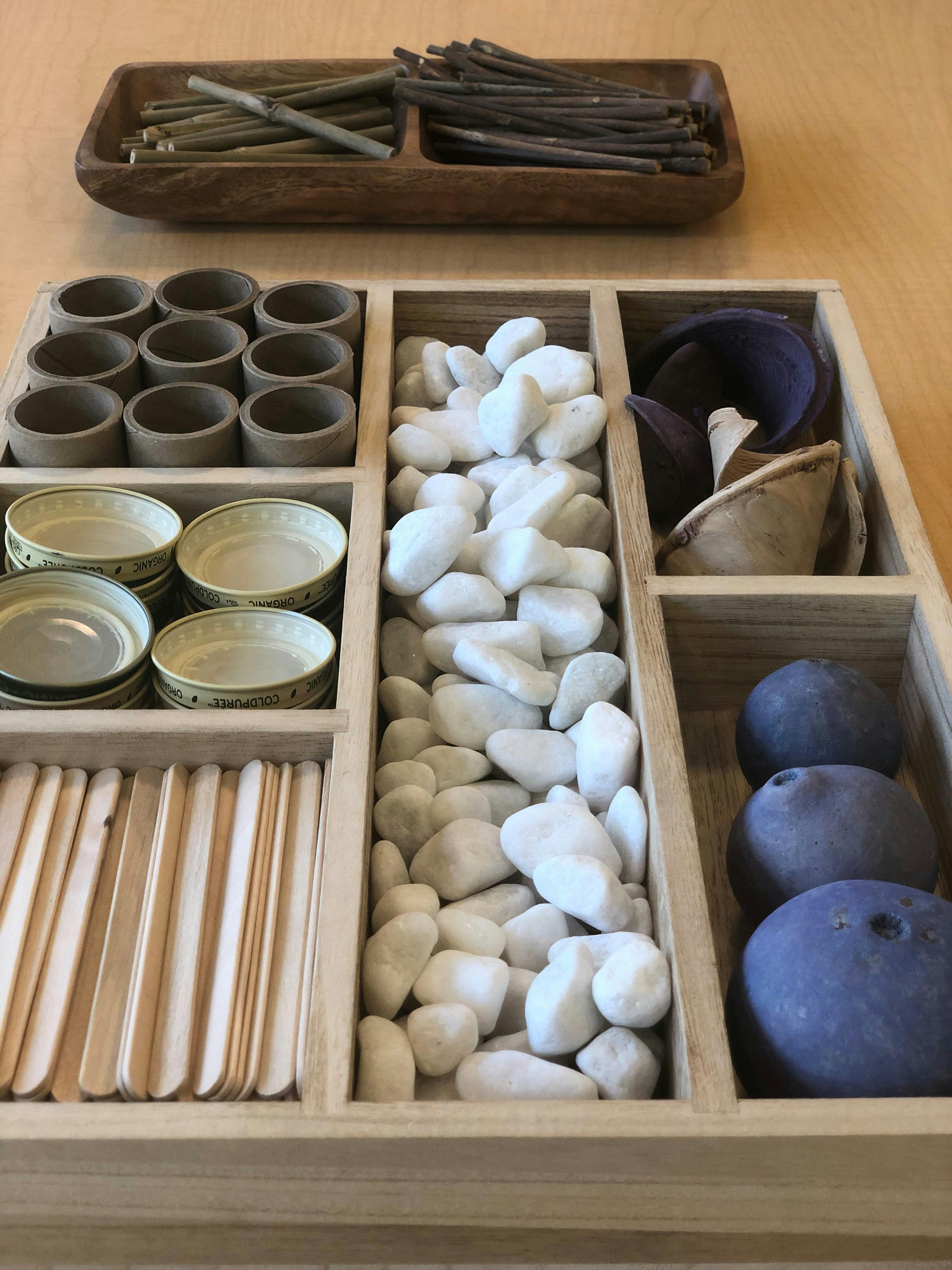 Wooden tray with various craft supplies including sticks, rings, bowls, stones