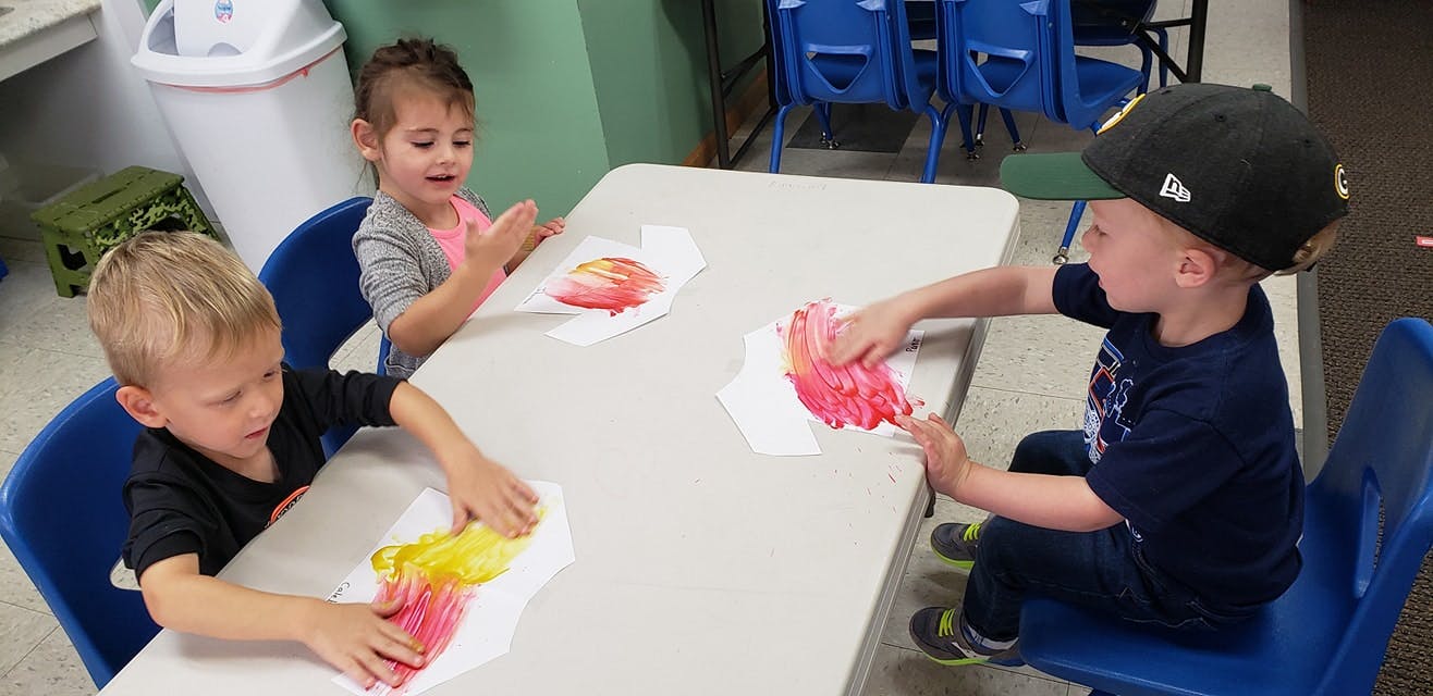 Three children doing finger painting at a table