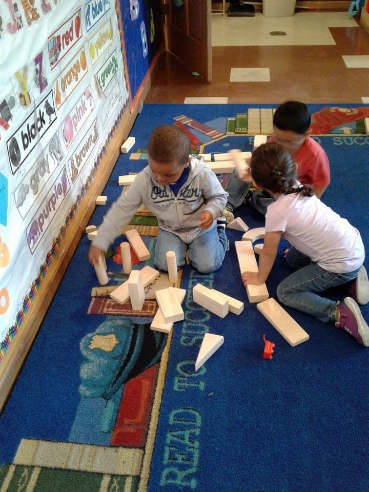 Three children playing with wooden blocks on a blue rug