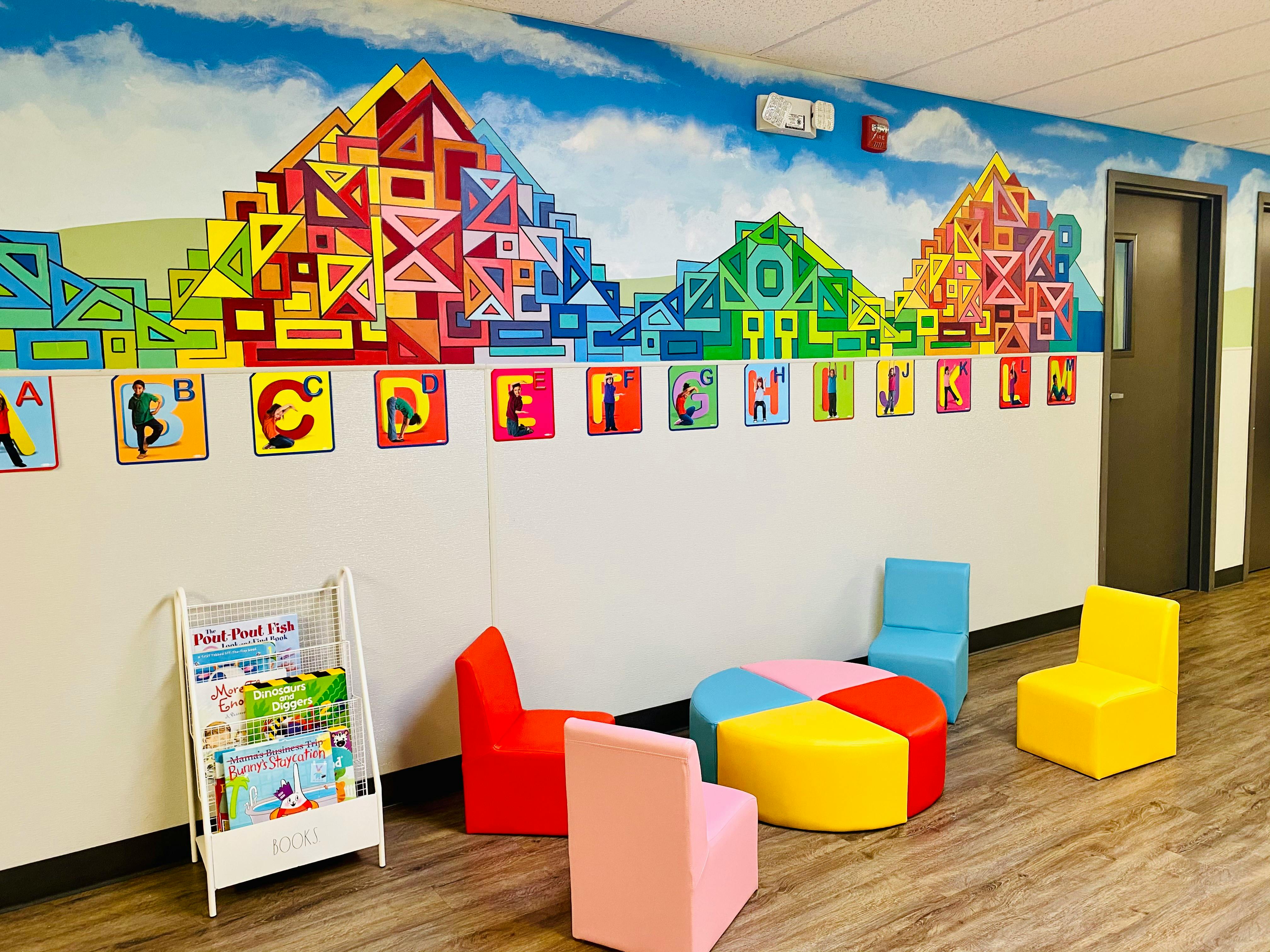 Children's room with colorful mural, ABC display, bright chairs, and a book rack