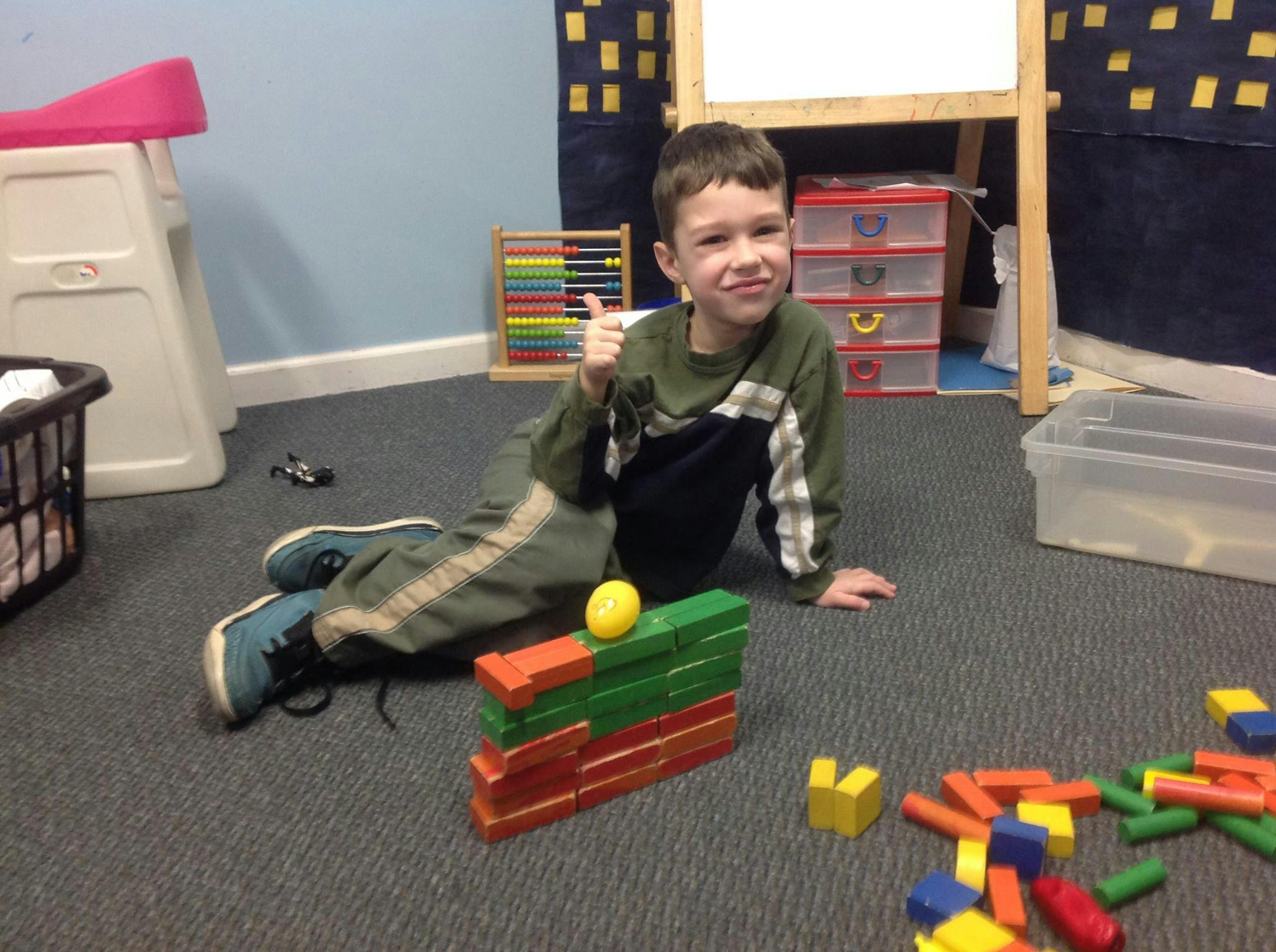 Child on floor with building blocks giving a thumbs up
