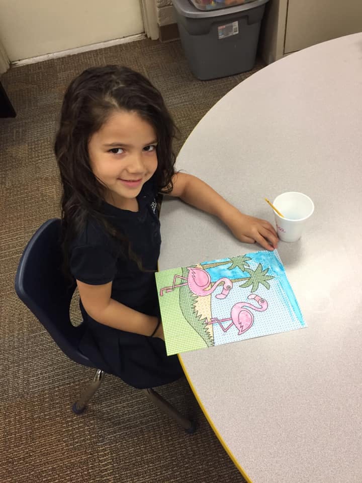 Child sitting at a table with a drawing of flamingos