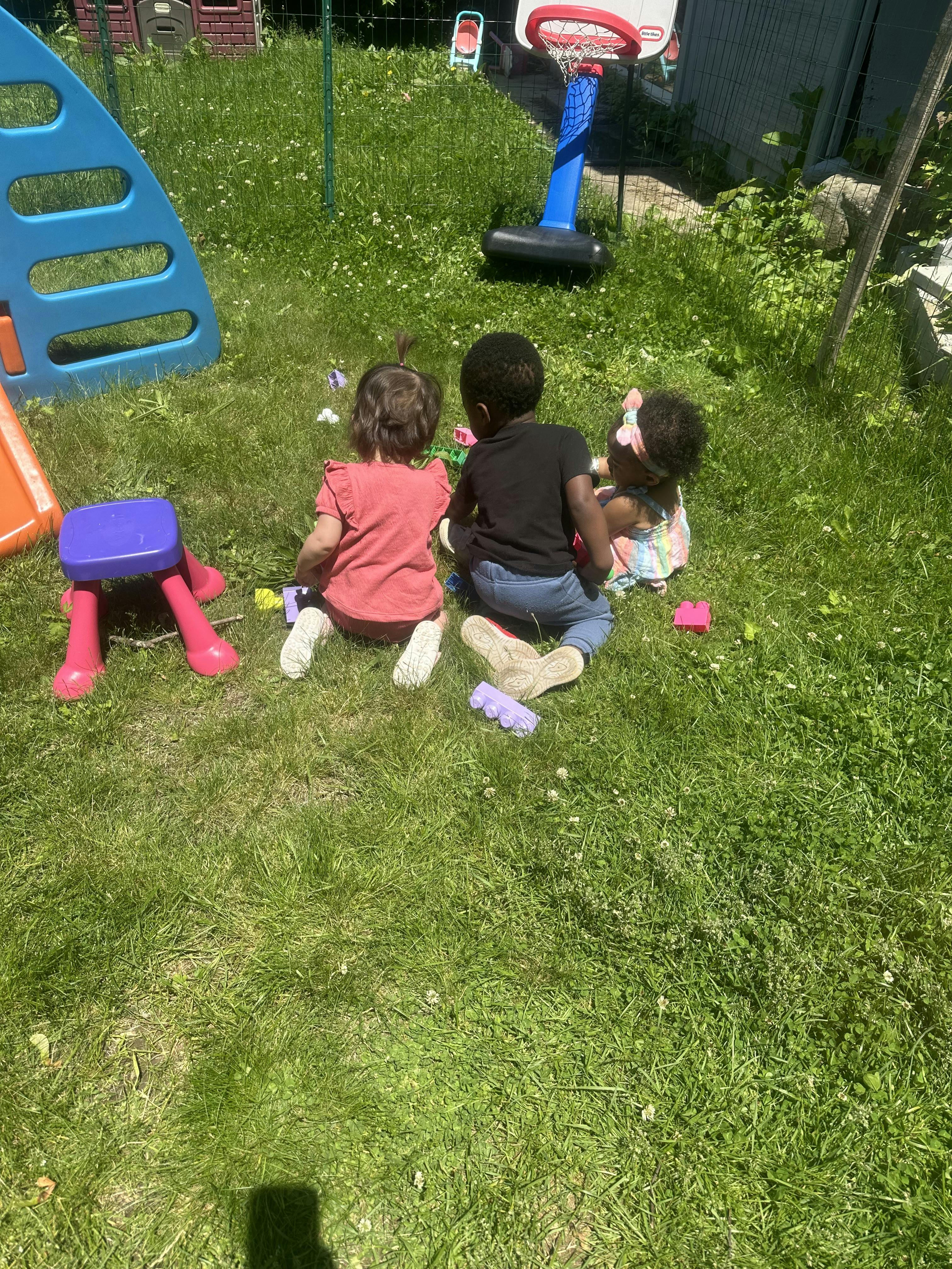 Three children sitting on grass playing with toys